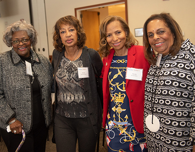 Four African American women stand together at a luncheon and smile at the camera