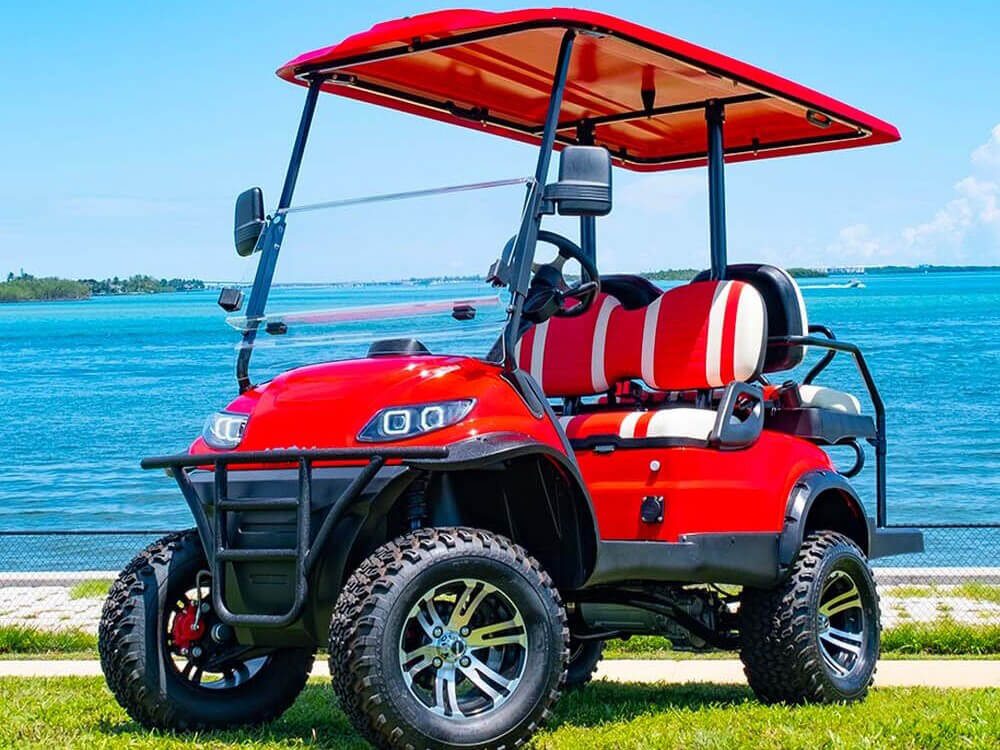A red golf cart sitting outside next to a large body of water.