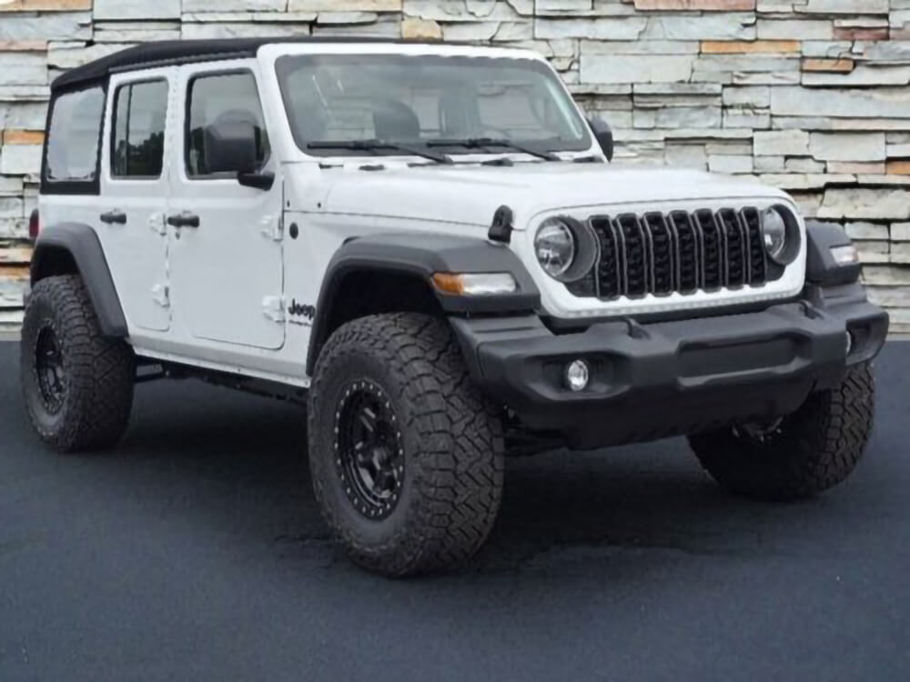 A white Jeep Wrangler parked next to a stone wall.