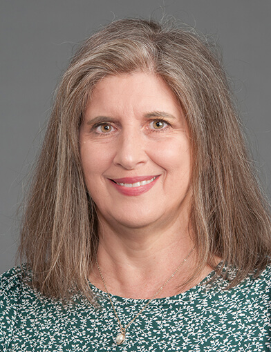 A woman with long hair wearing a green shirt smiling at the camera.